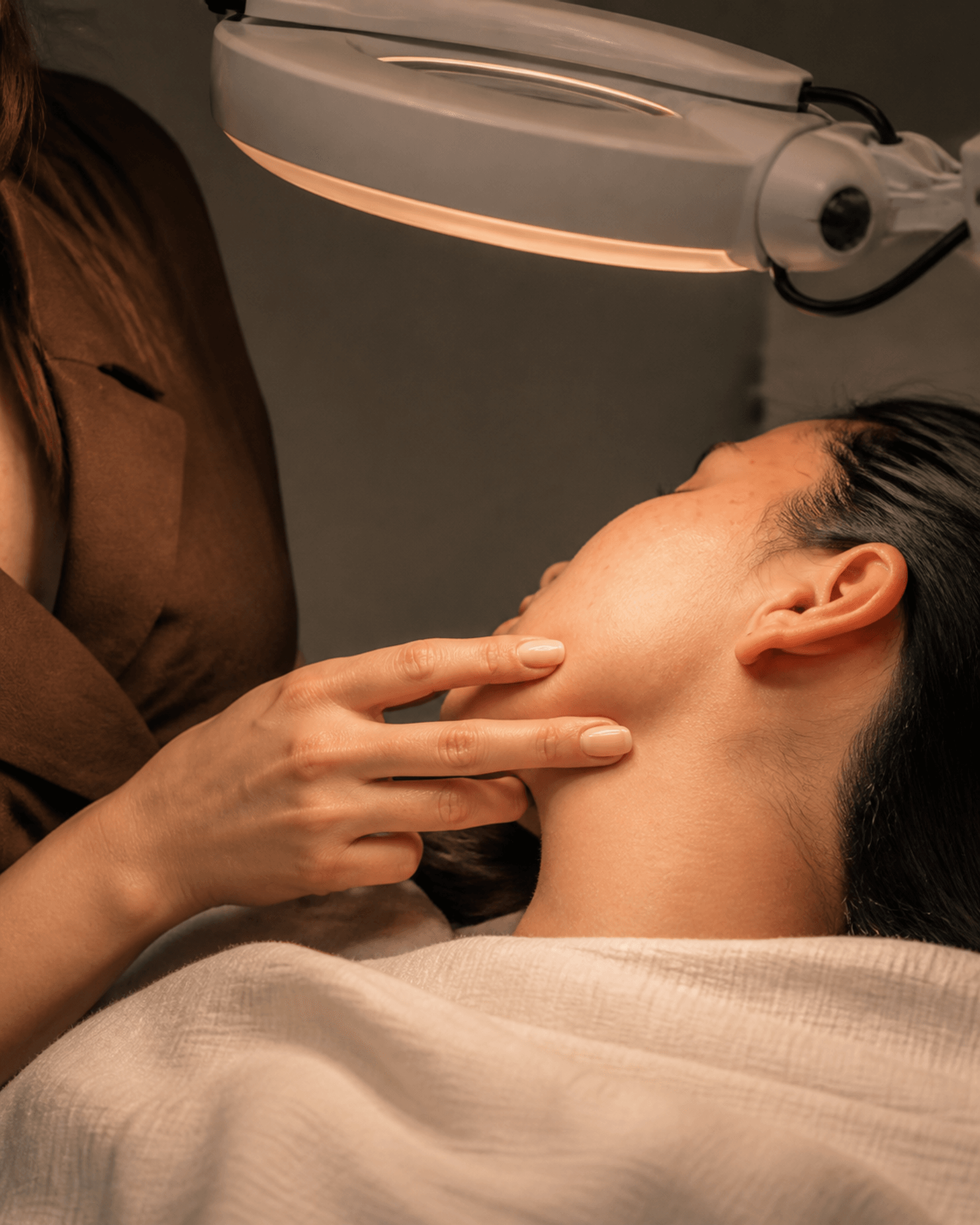 A hand gently turns an anonymous cheek beneath a magnifying lamp