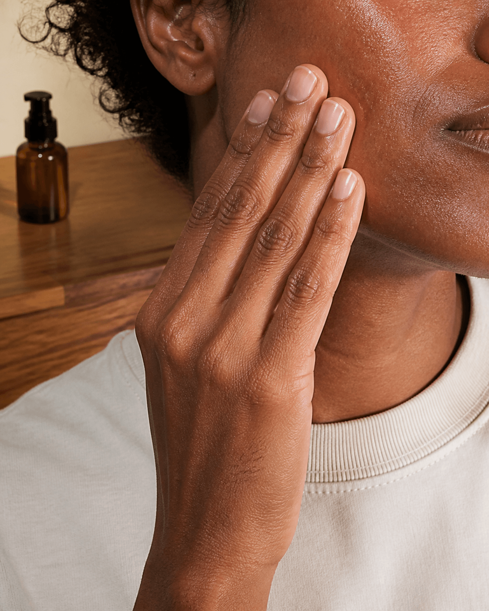 A person presses serum into their cheek beside an unlabeled amber pump