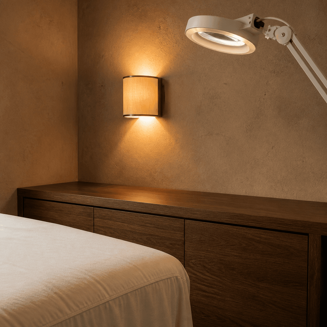 An ivory treatment bed, walnut cabinetry, and a magnifying lamp in a warm mineral room